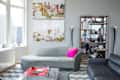 Modern living room with gray sofa, pink pillow, glass coffee table, and decorative shelving unit.