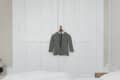 Gray sweater on a hanger against white paneled doors in a minimalist bedroom.