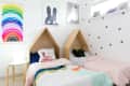 Children's bedroom with two house-shaped beds, colorful bedding, rainbow poster, and playful wall art.