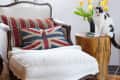 White armchair with Union Jack pillow, wooden side table, yellow tulips, and a black and white cat sitting beside.