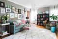 Eclectic living room with gallery wall, teal sofa, floral cushions, bookshelf with globes, and a large white rug.
