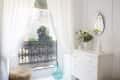 White dresser with a decorative mirror, vase of yellow flowers, and candles near a window with sheer curtains and ornate railing.
