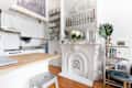 White kitchen with wooden countertop, ornate fireplace, open shelves, and a small table with books and a plant.