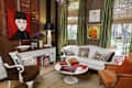 Eclectic living room with white sofa, colorful portraits, green curtains, and a round coffee table with books and flowers.