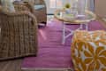 Wicker chairs and a glass coffee table on a purple rug in a sunroom with blue walls and French doors.