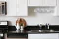 Modern kitchen with white cabinets, black countertop, hanging mugs, wooden utensils, and a small potted cactus.