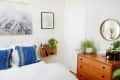 Bedroom with blue patterned pillows, wooden dresser, plants, and wall art.