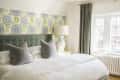 Bedroom with a large bed, green headboard, floral wallpaper, and a white lamp on a side table.