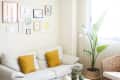 Living room with a white sofa, yellow cushions, white coffee table, potted plants, and a gallery wall.
