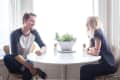 Two people sitting at a round white table with a potted plant, under a silver arc lamp.