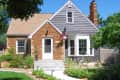 Brick and gray siding house with American flag, surrounded by green lawn and shrubs, under a clear blue sky.