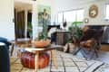 Living room with a wooden coffee table, leather pouf, plants, and a butterfly chair on a geometric rug.