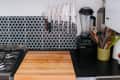 Kitchen corner with a wooden cutting board, knife rack, blender, and utensils against a geometric tile backsplash.