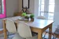 Dining room with wooden table, white and black chairs, pink pendant light, and potted plants on a beige rug.