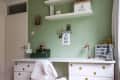 White desk with gold polka dots, green wall, shelves, lamp, and decor items including a lightbox and small deer figurine.
