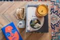 Coffee table with a candle, coasters, a book titled "The Girls," and a bowl of matchbooks on a patterned rug.