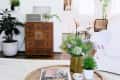 Living room with round wooden coffee table, books, plants, and a vintage cabinet. Dining area visible in the background.