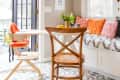 Cozy breakfast nook with a wooden chair, high chair, patterned floor, and colorful cushions on a window seat.