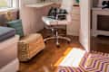 Home office nook with white desk, swivel chair, storage boxes, and decor in a closet space with open doors.