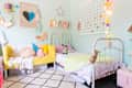 Children's bedroom with pastel decor, twin beds, yellow sofa, colorful pillows, and string lights on a mint green wall.