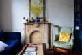Cozy living room with blue sofa, ornate fireplace, green armchair, and yellow floral pillow.