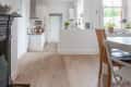 Open-plan kitchen and dining area with wooden floors, white walls, a round table, and potted plants by the window.