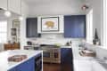 Modern kitchen with blue cabinets, marble countertops, a large stove, and framed pig artwork above.