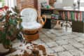 Cozy home office with brick walls, wicker chair, desk with laptop, books, and a potted plant by a large window.