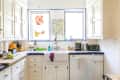 Bright kitchen with white cabinets, blue tile counters, farmhouse sink, coffee maker, and colorful window decor.
