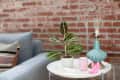 Blue sofa with a patterned pillow next to a white table holding a potted plant, pink mug, and turquoise lamp, against a brick wall.