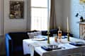 Cozy dining area with a blue sofa, white tablecloth, gold candlesticks, and wine bottle on a table by a window.