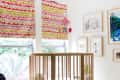 Nursery with a round wooden crib, colorful blinds, striped yellow rug, and wall art.