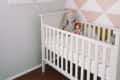 White crib with polka dot bedding, stuffed bunny, and doll in a nursery with geometric accent wall and framed animal prints.
