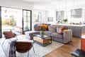 Open-plan living room with gray sectional sofa, colorful cushions, glass coffee table, and kitchen in the background.