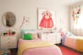 Two colorful twin beds in a bright room with a dresser, round mirror, and framed hanbok artwork.