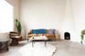 Mid-century modern living room with tan sofa, blue and red pillows, cactus, wicker chair, and white fireplace.