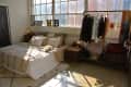 Loft bedroom with a cozy bed, a cat, large windows, and a clothing rack with various garments and accessories.