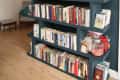 Dark blue bookshelf filled with books, glass jars, and decor items, set against a wooden floor and white wall.