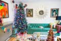 Colorful living room with a decorated Christmas tree, green sofa, vibrant artwork, and a sunburst mirror on the wall.