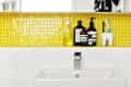 Bathroom sink with yellow tile backsplash, mirrored cabinet, toiletries, and toothbrush holder.