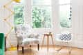 Floral armchair, yellow lamp, and white rocking chair with chevron pillow in a bright room with large windows and wooden floor.