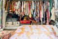 Open closet with colorful clothes, hats, and suitcases; floral bedspread in foreground.