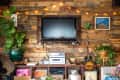 Rustic living room with wood panel wall, mounted TV, string lights, plants, guitar, and vinyl records on a shelf.