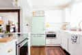Bright kitchen with mint green fridge, white cabinets, wooden floor, and decorative rug.