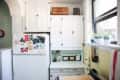 White kitchen with cabinets, fridge covered in photos, potted plants on windowsill, and yellow tiled backsplash.