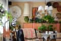 Eclectic living room with plants, abstract art, woven decor, and a rope chandelier over a white table.