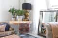 Cozy living room corner with plants on a round table, a large mirror, patterned chair, and a plush sofa.