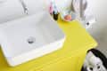 Yellow bathroom vanity with white sink, striped towel, toothbrushes, and rubber ducks on bathtub ledge.