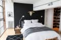 Modern bedroom with black accent wall, white bedding, gray throw, bedside lamps, and a wall-mounted bull skull.