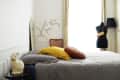 Bedroom with a gray bedspread, yellow and round pillows, a mannequin, and a rabbit lamp on a side table.